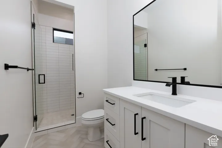 White vanity with integrated rectangular sink and quartz countertop, matte black hardware and fixtures, framed wall mirror, walk-in shower with vertical tile surround, and herringbone-patterned flooring