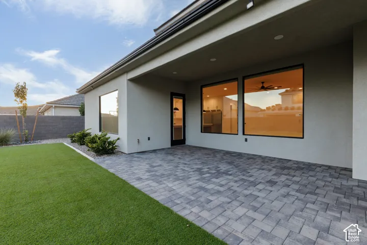 Covered concrete paver patio with recessed lighting, synthetic turf lawn, and exterior stucco finish