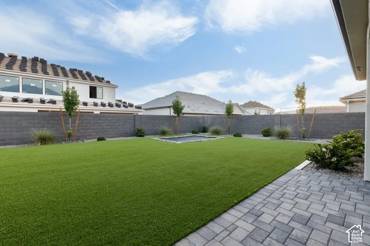 Private backyard featuring synthetic turf, paver patio, masonry perimeter wall, and in-ground trampoline