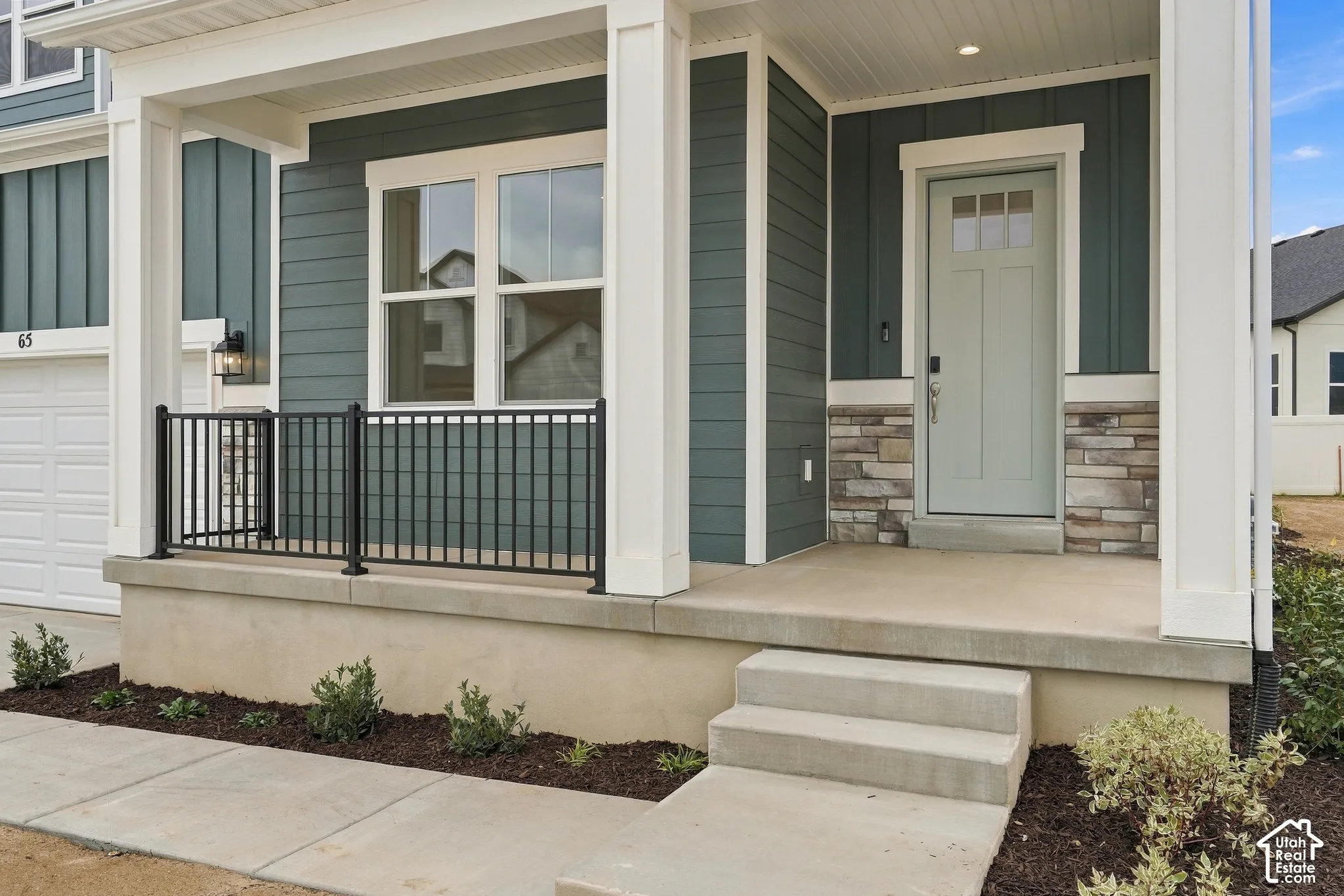 Exterior featuring lap and vertical siding, stacked stone veneer accents, a covered concrete porch, and black metal railing