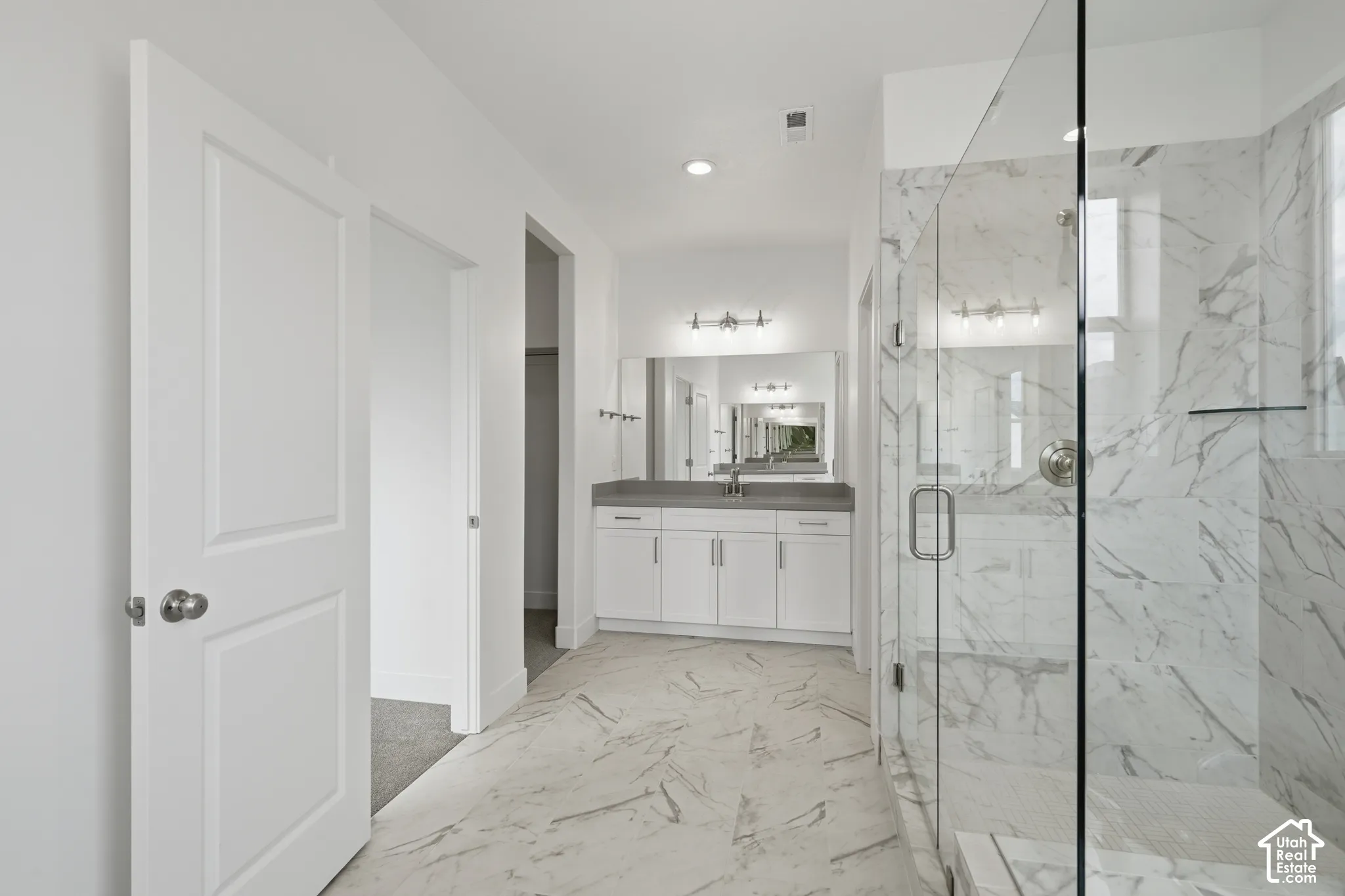 Bathroom featuring white cabinetry, solid-surface countertop, frameless glass shower enclosure with floor-to-ceiling tile surround, and large-format tile flooring