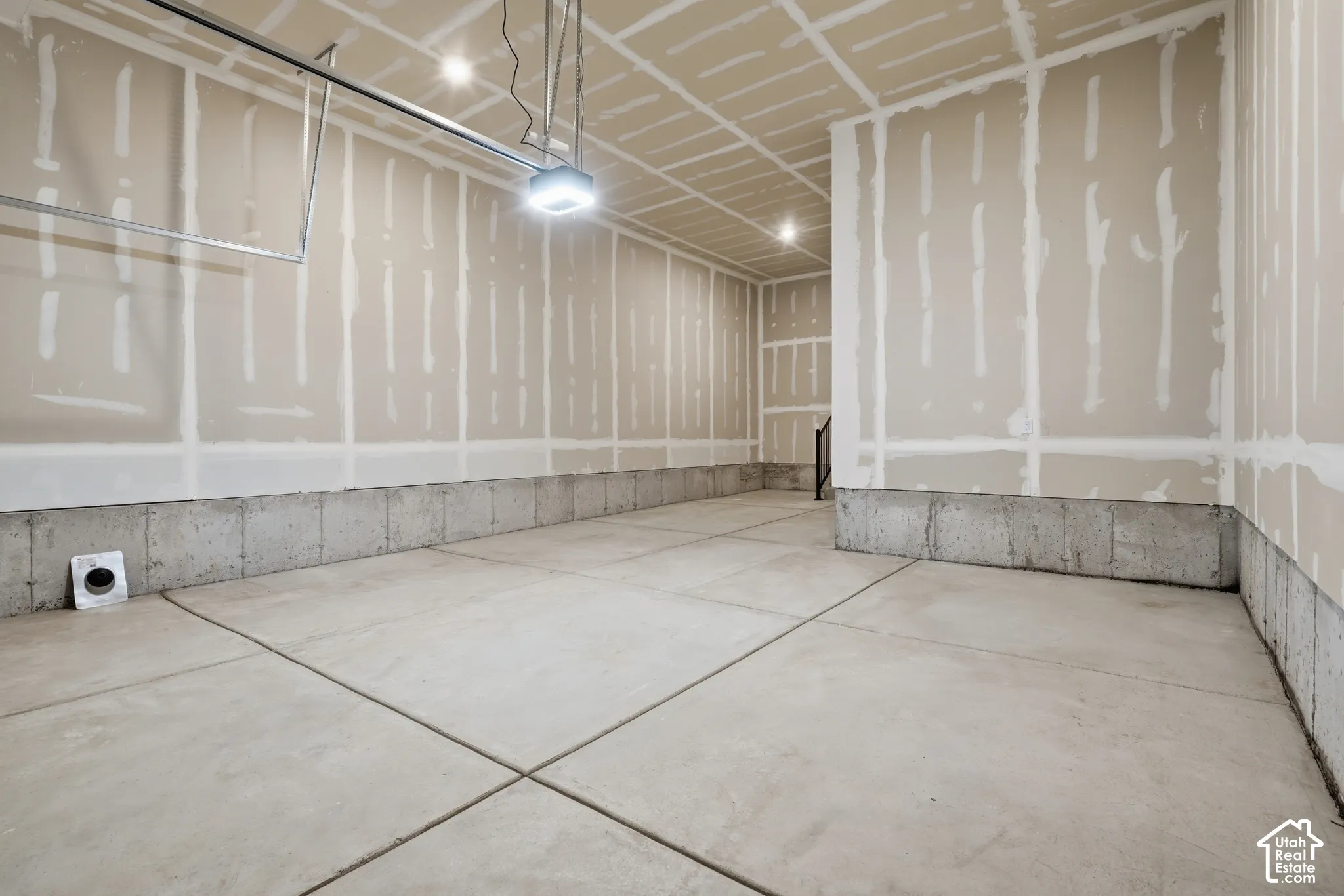 Unfinished garage interior featuring concrete flooring, concrete foundation walls, and taped drywall