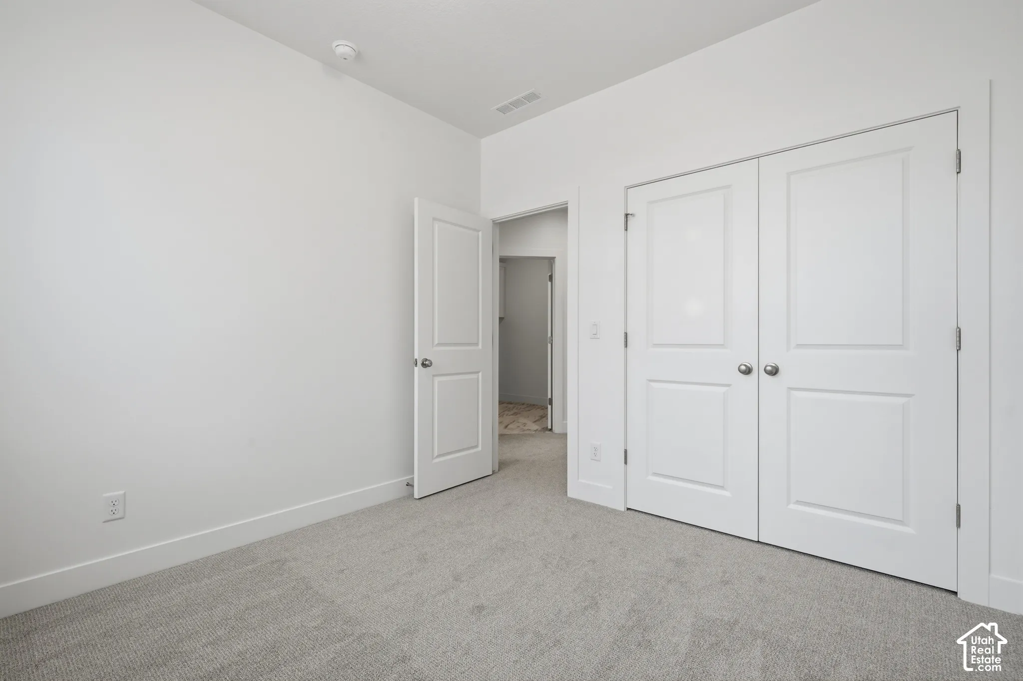 Interior space featuring neutral-toned carpeting, white walls, double-door closet with brushed nickel hardware, and a solid-core interior door