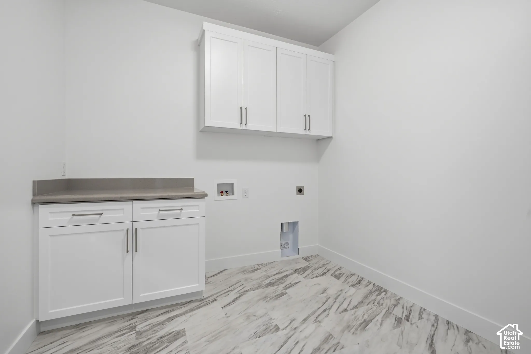 Utility space featuring white shaker-style cabinetry, solid-surface countertop, upper storage cabinets, and stone-patterned tile flooring