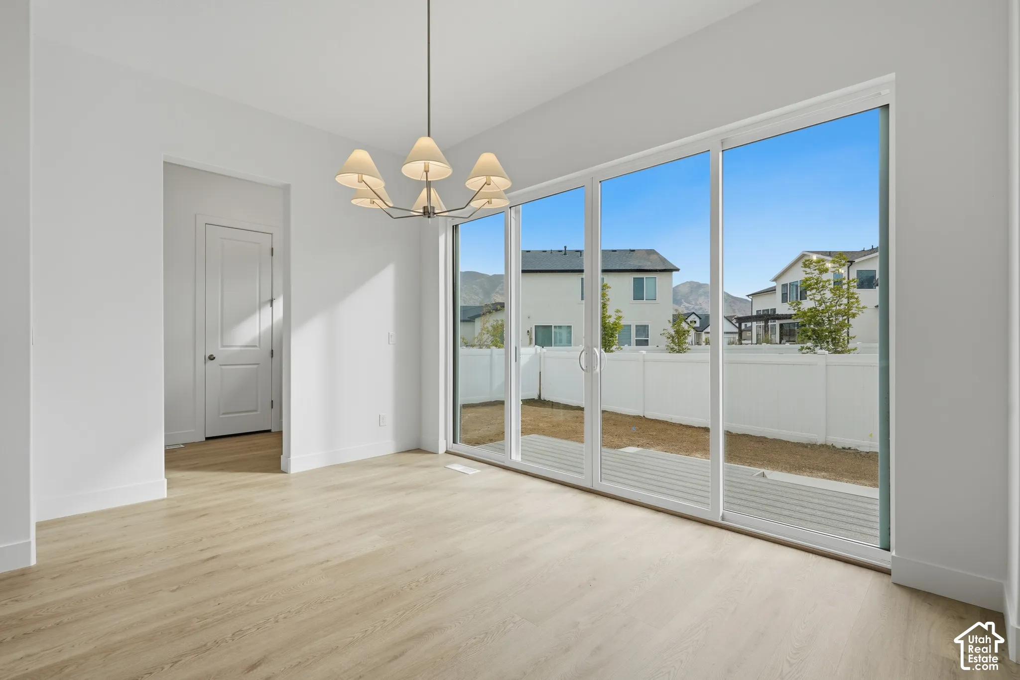 Wood-finish flooring, multi-panel sliding glass doors, metal chandelier with fabric shades, and white interior door