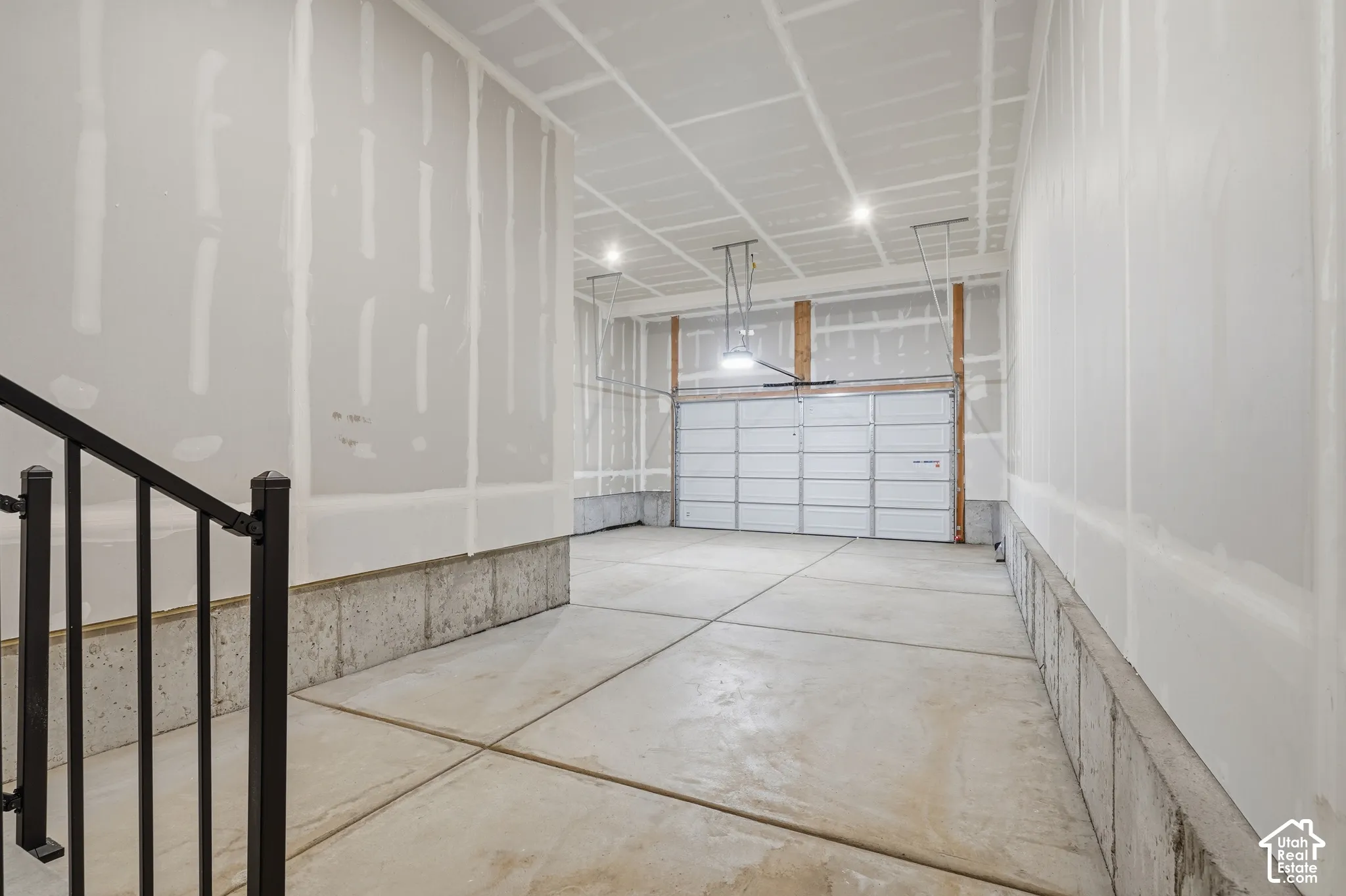Attached garage with concrete flooring, finished drywall, overhead lighting, and metal handrail