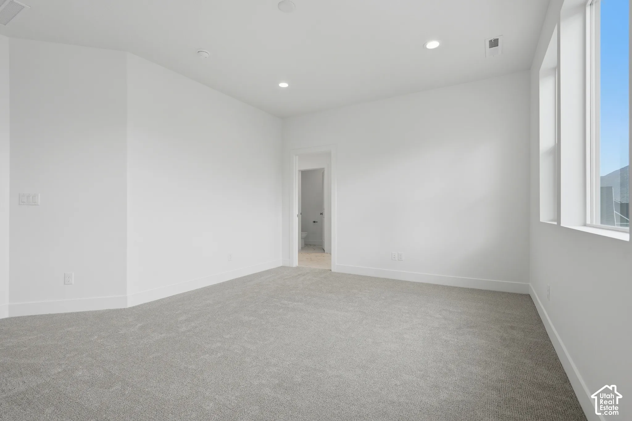 Neutral-toned wall-to-wall carpeting, recessed ceiling lighting, large windows, and crisp white wall finishes