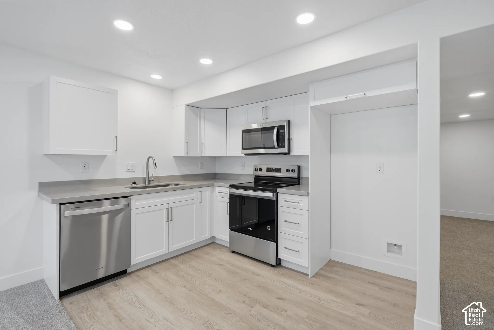 Kitchen featuring white Shaker-style cabinetry, solid-surface countertops, recessed ceiling lighting, wood-finish flooring, and stainless steel appliances