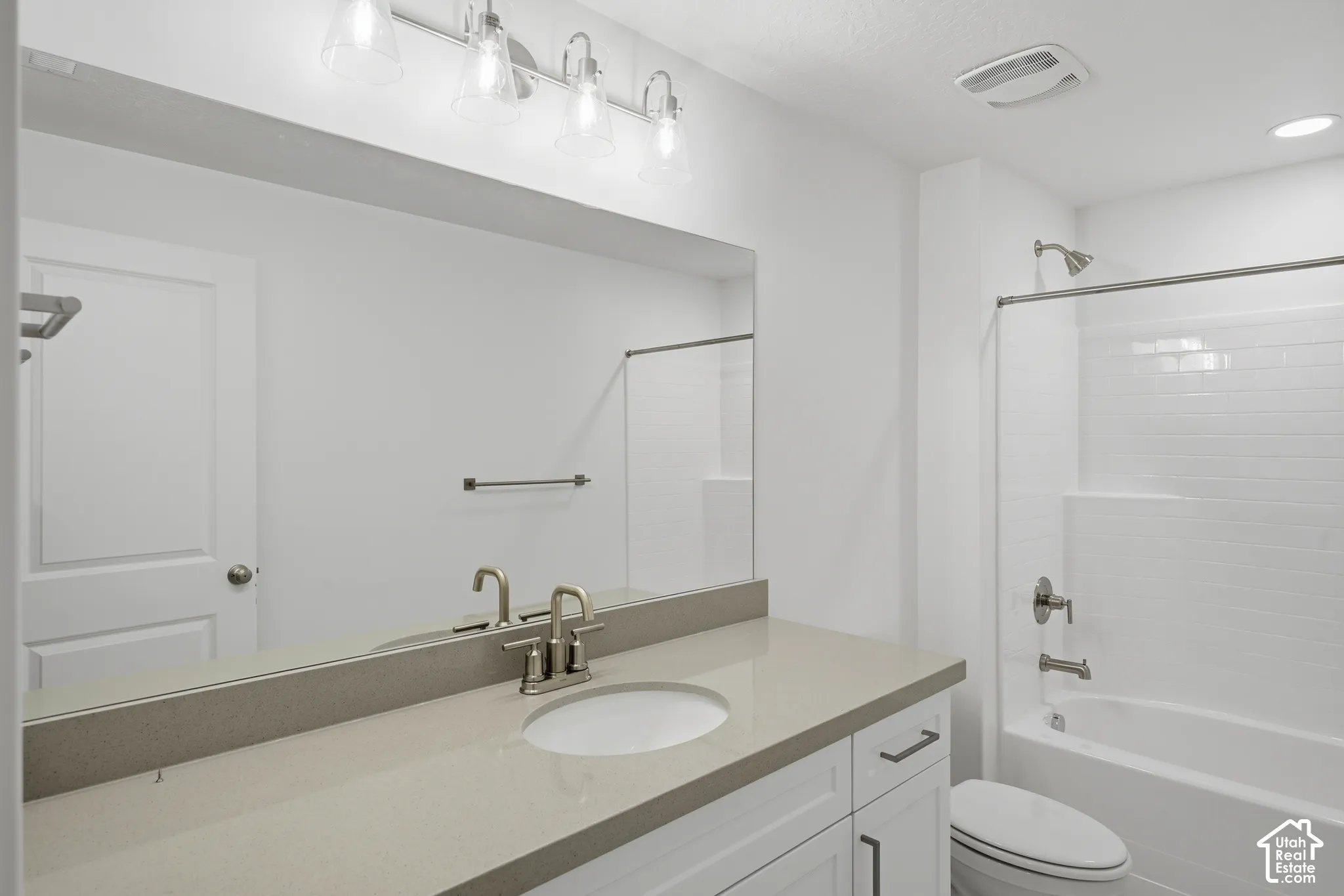 Bathroom featuring a vanity with a solid-surface countertop, an oval under-mount sink, white cabinetry with dark hardware, a full-width mirror, and a tub-shower combination with subway-style tile surround