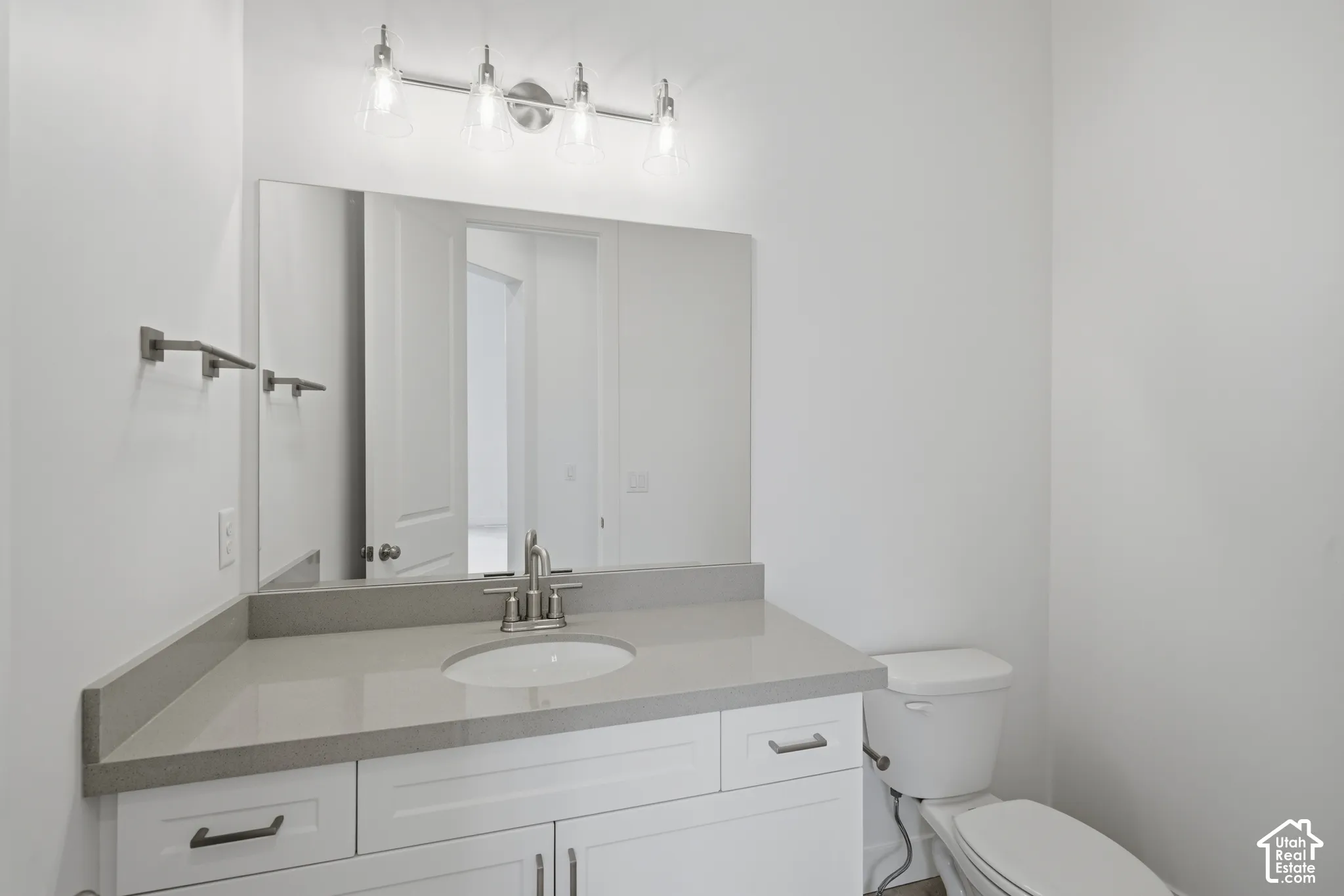 Bathroom featuring a white shaker-style vanity with neutral stone-finish countertop, undermount sink, four-light vanity fixture, and large-format wall mirror