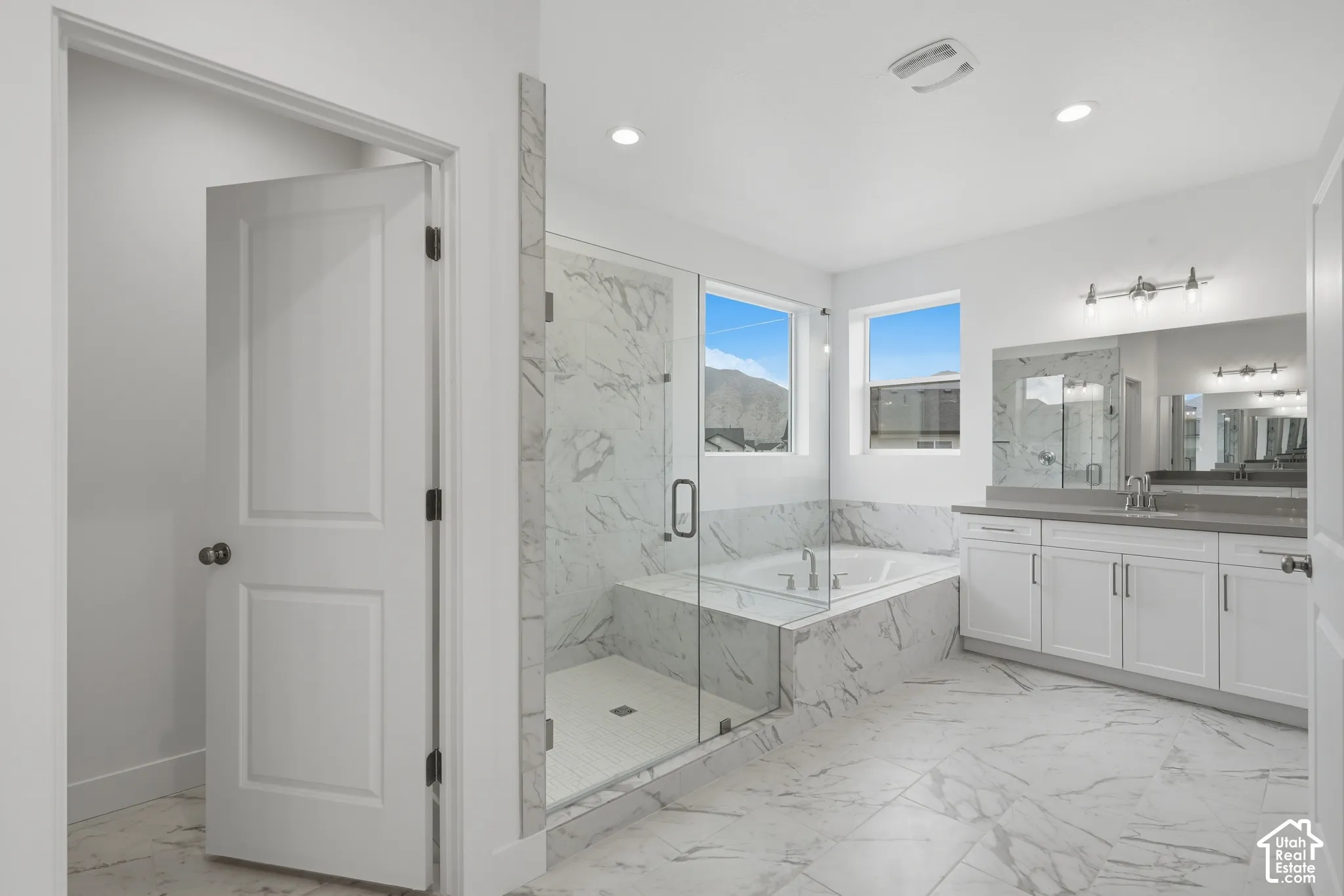Glass-enclosed shower with stone-finish surround, built-in soaking tub, dual-sink vanity with stone-finish countertop, and stone-finish floor tile