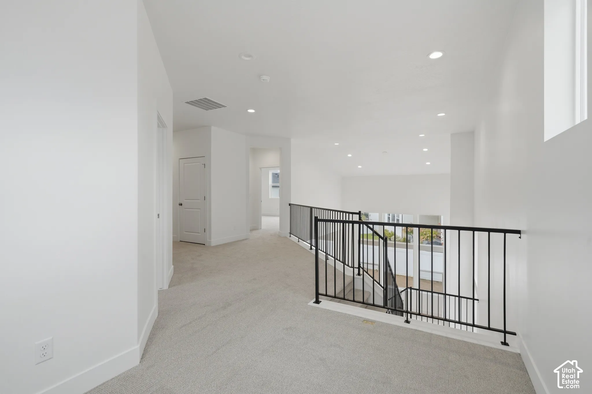 Neutral interior landing featuring carpeted flooring, recessed lighting, and a black metal railing