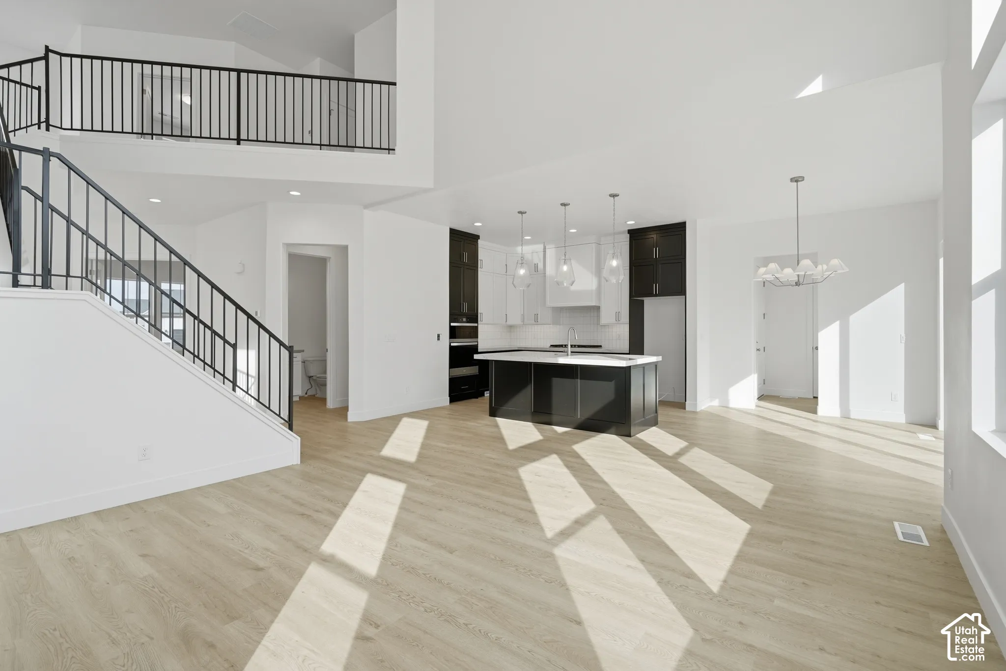 Open-concept interior featuring high ceilings, wood-finish flooring, a center kitchen island with contrasting cabinetry, and an iron stair railing
