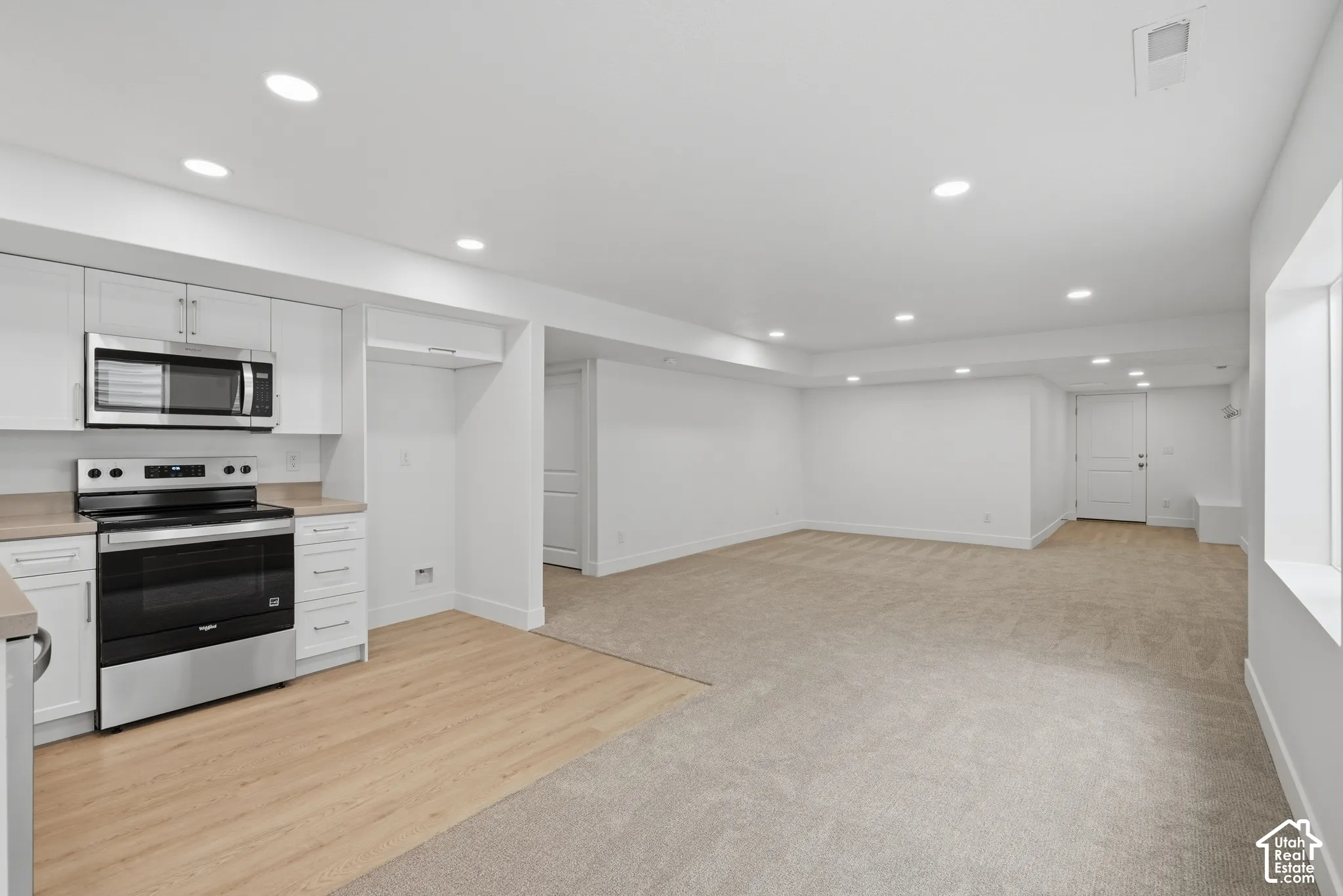Kitchen area featuring white cabinetry, integrated stainless steel microwave, and freestanding stainless steel range with wood-finish flooring and recessed lighting