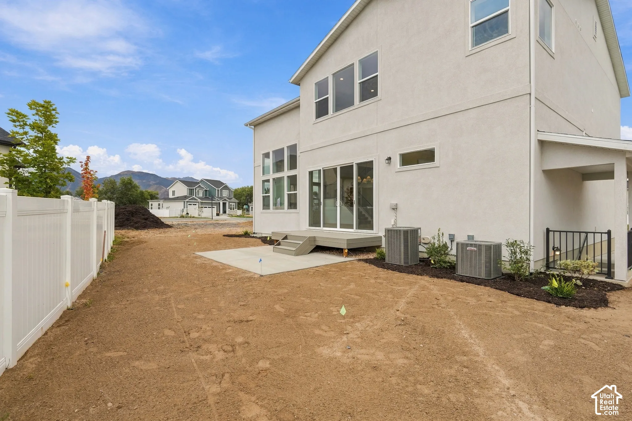 Two-story exterior featuring light-colored stucco siding, large multi-pane windows, sliding glass door, elevated concrete patio, and a white vinyl privacy fence