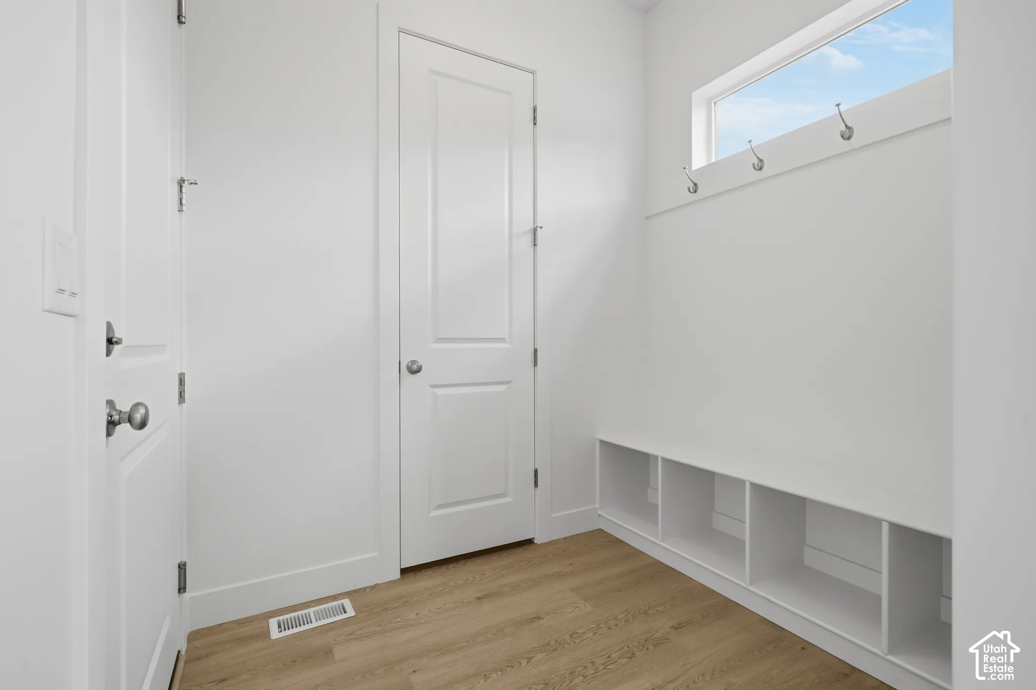 Mudroom featuring wood-finish flooring, custom built-in cubby storage, wall-mounted metal hooks, a horizontal transom window, and solid core doors with brushed nickel hardware