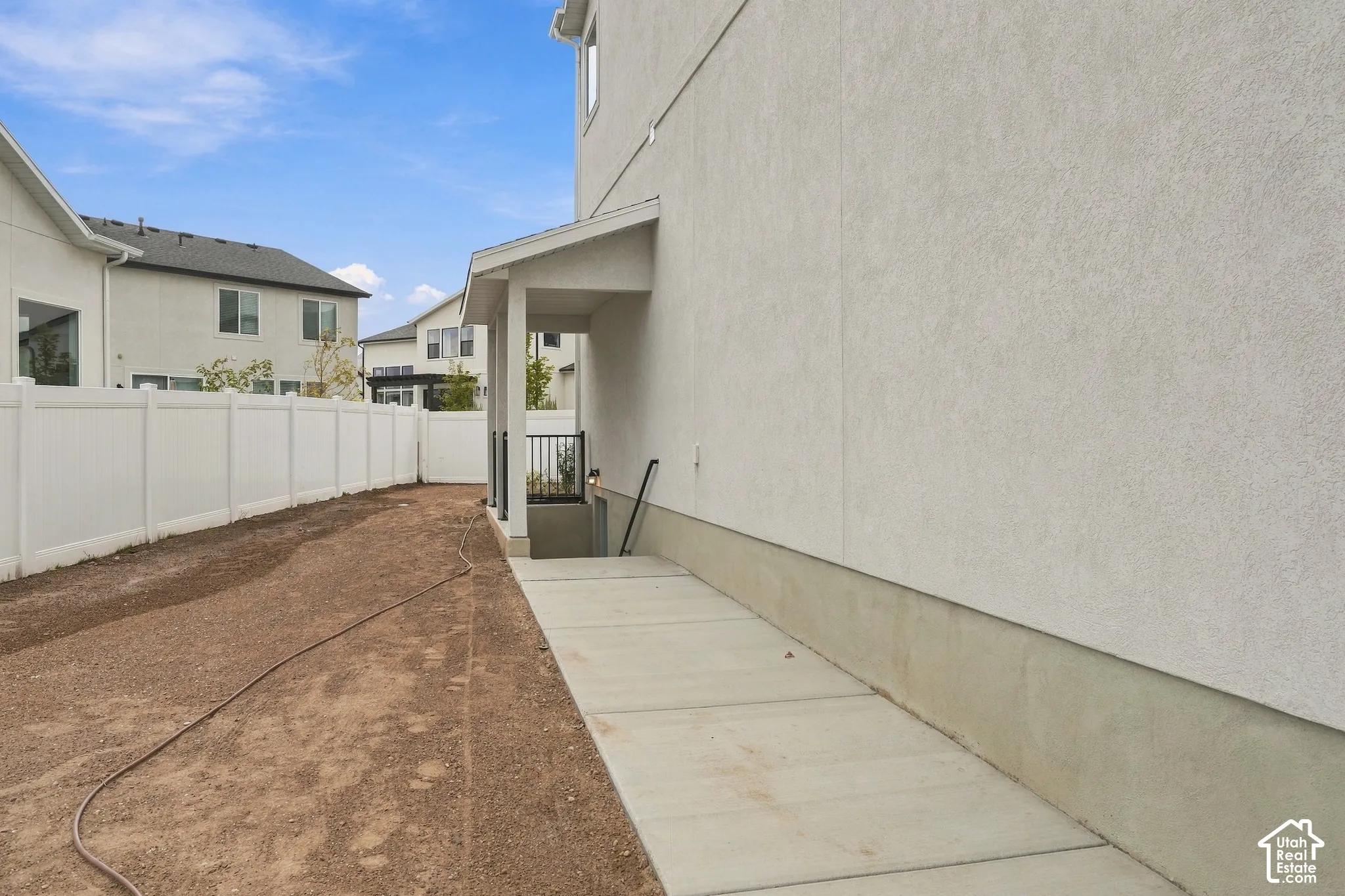 Stucco exterior featuring a concrete walkway, basement stairwell access, and white vinyl perimeter fencing