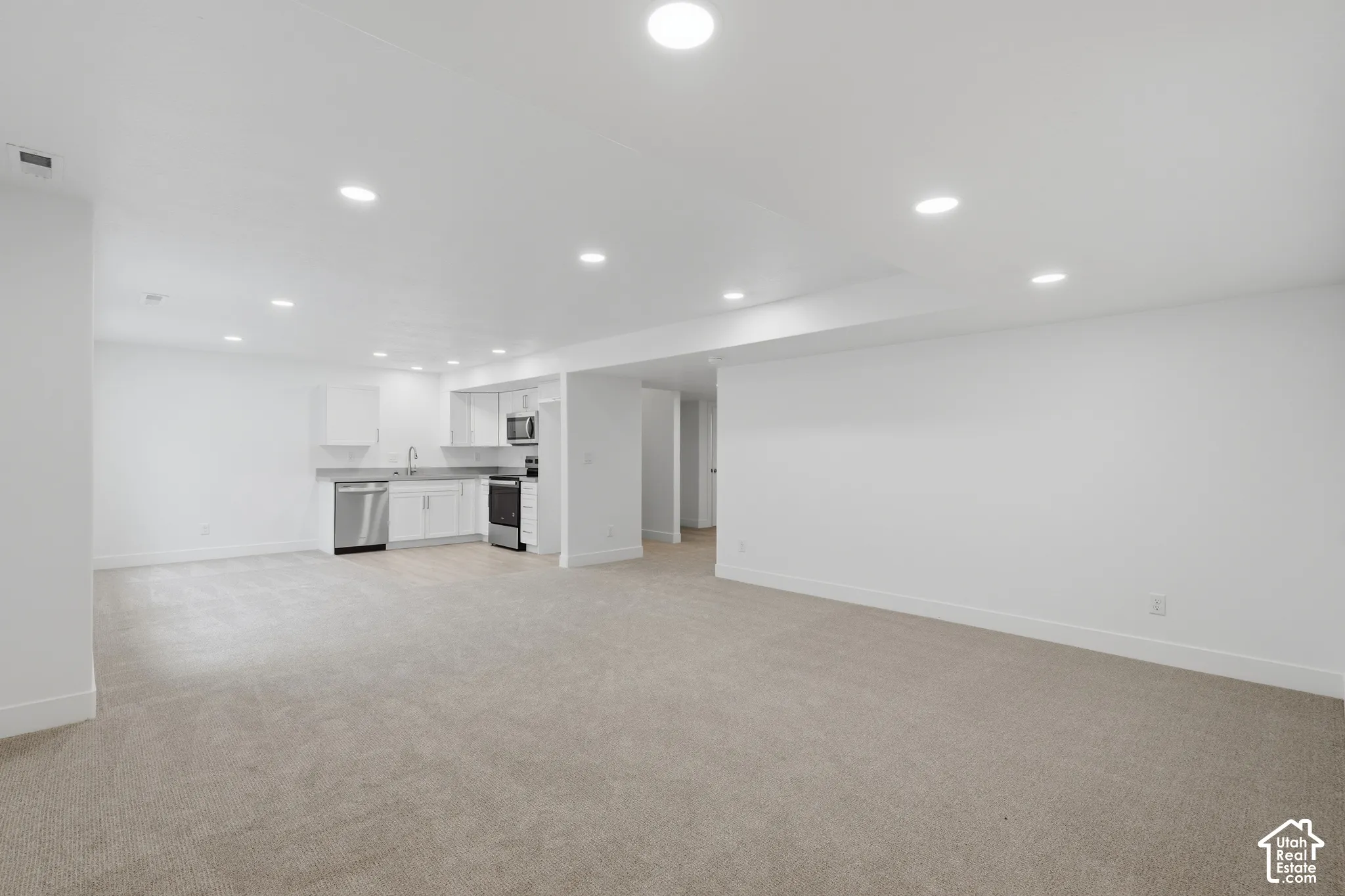Open concept interior featuring recessed lighting, wall-to-wall carpeting, and a kitchen area with white cabinetry, stainless steel appliances, and a solid surface countertop