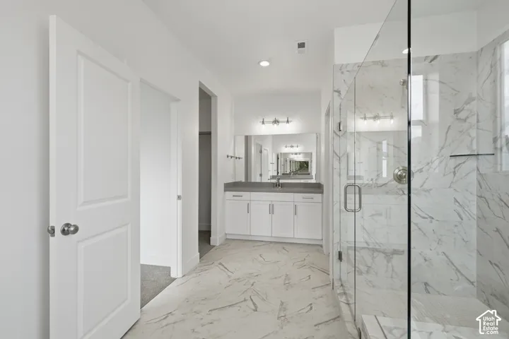 Bathroom featuring white cabinetry, solid-surface countertop, frameless glass shower enclosure with floor-to-ceiling tile surround, and large-format tile flooring