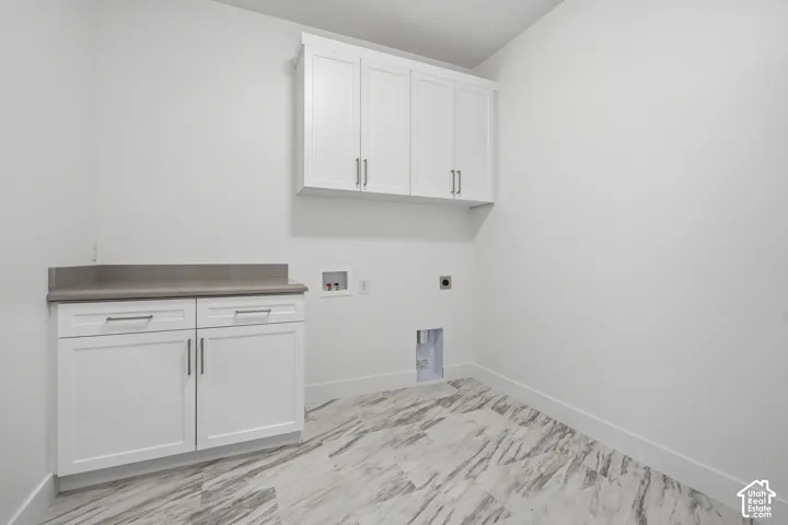 Utility space featuring white shaker-style cabinetry, solid-surface countertop, upper storage cabinets, and stone-patterned tile flooring