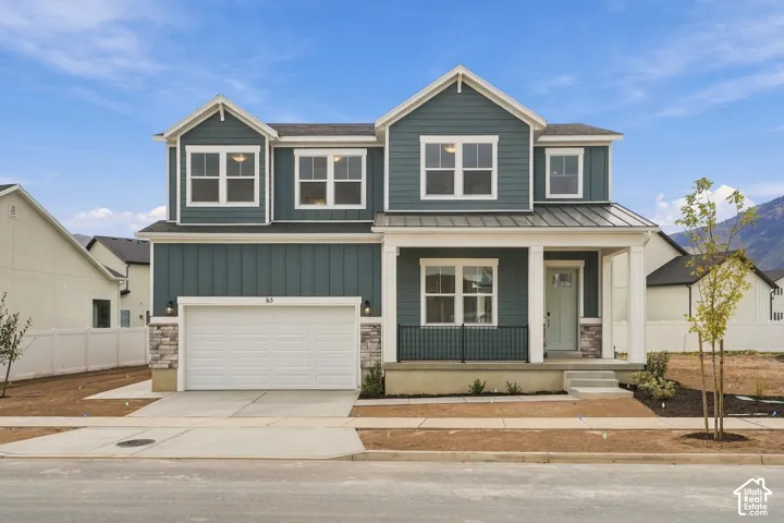 Two-story residence featuring horizontal and vertical lap siding, a metal roof porch accent, a stone-veneer foundation finish, and an attached two-car garage