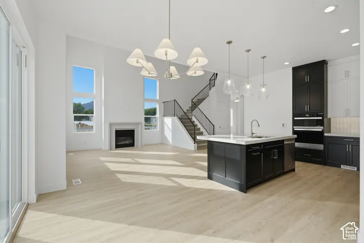 Open-concept interior featuring light wood-finish flooring, two-story windows, a fireplace with a minimalist mantel, a center kitchen island with quartz countertops, and a staircase with metal railings