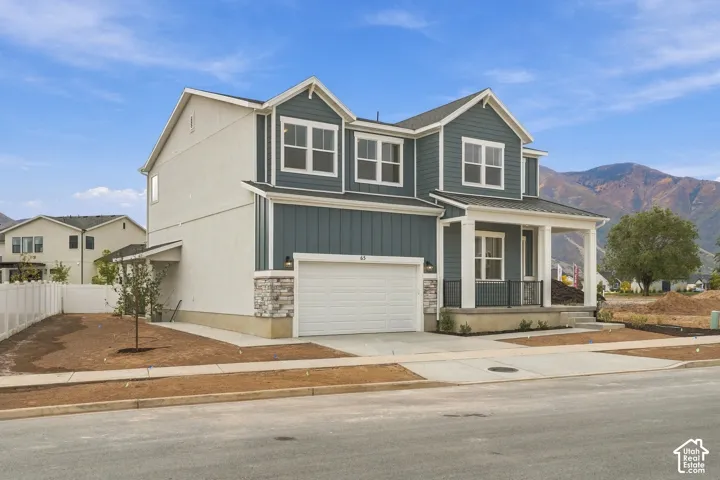 Two-story exterior featuring board-and-batten siding, stone masonry accents, a covered front porch with square columns, and a two-car garage