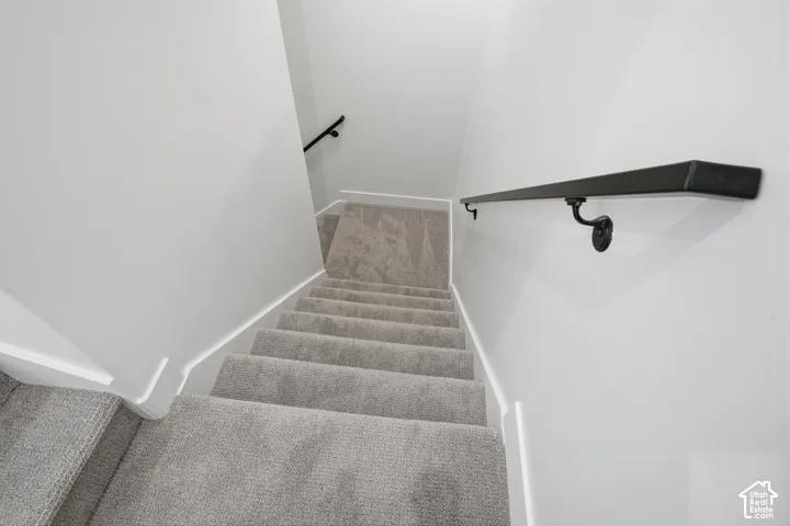 Staircase featuring neutral-toned carpeting, matte black wall-mounted handrails, and clean white walls