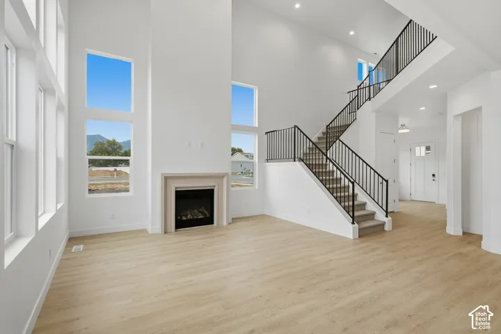 Double-height ceilings, floor-to-ceiling windows, built-in fireplace with a surround, wood-finish flooring, and a staircase with a matte black metal railing