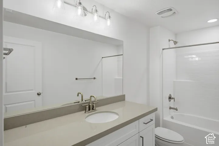 Bathroom featuring a vanity with a solid-surface countertop, an oval under-mount sink, white cabinetry with dark hardware, a full-width mirror, and a tub-shower combination with subway-style tile surround