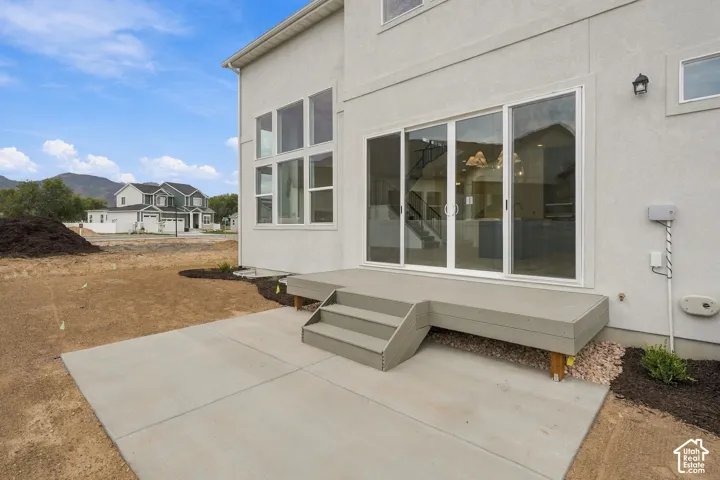 Stucco exterior with oversized windows, sliding glass door, elevated wood-finish deck, and poured concrete patio