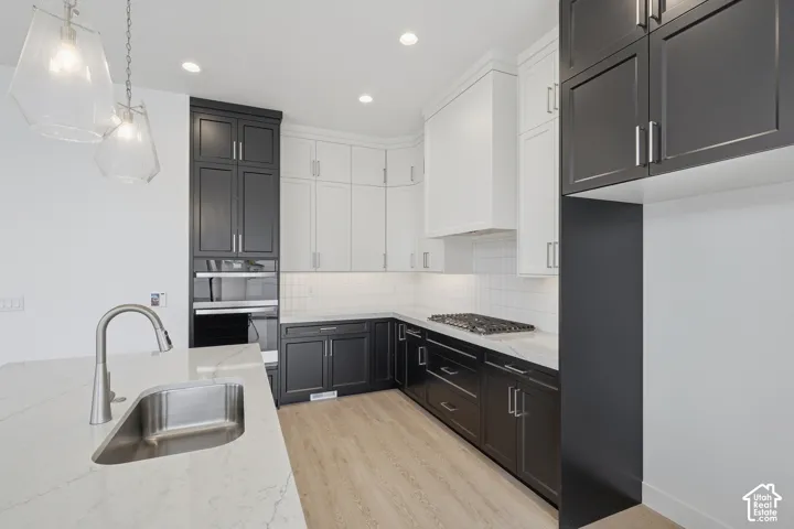 Kitchen featuring two-tone custom cabinetry, quartz countertops, integrated stainless steel gas cooktop, built-in double wall ovens, and geometric glass pendant lighting