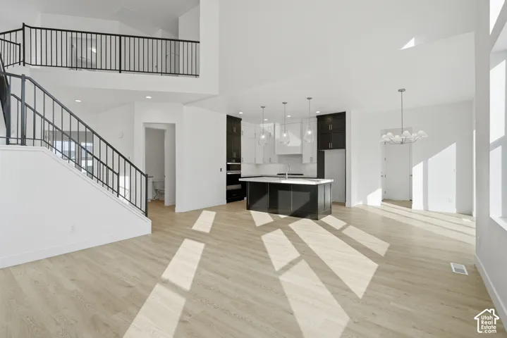 Open-concept interior featuring high ceilings, wood-finish flooring, a center kitchen island with contrasting cabinetry, and an iron stair railing