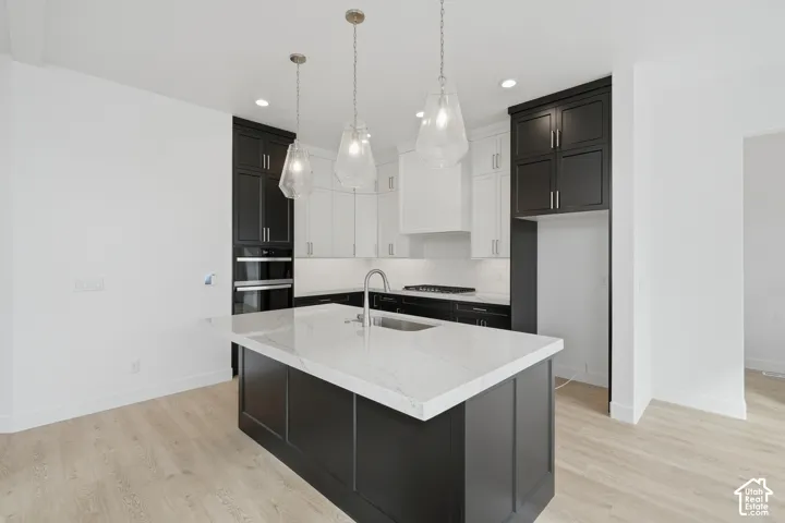 Kitchen featuring two-tone cabinetry, a central island with a stone-finish countertop, stainless steel double wall ovens, a gas cooktop, and glass pendant lighting