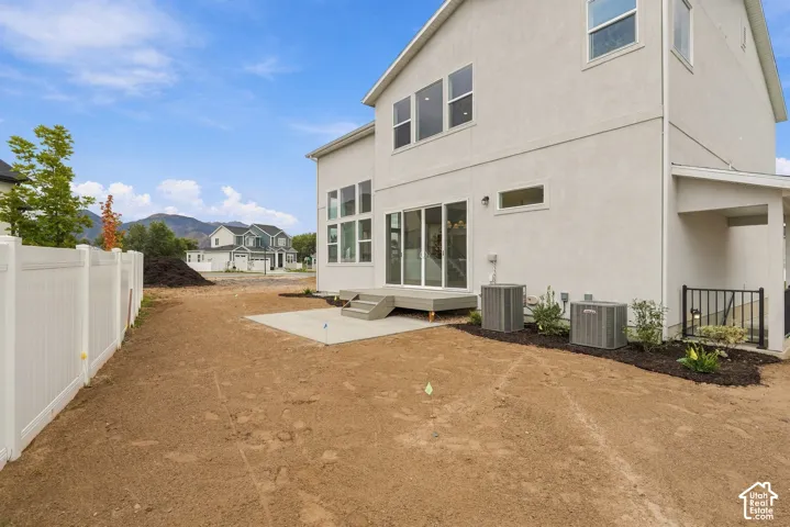 Two-story exterior featuring light-colored stucco siding, large multi-pane windows, sliding glass door, elevated concrete patio, and a white vinyl privacy fence