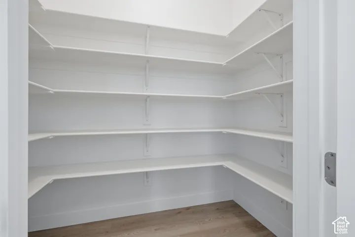 Walk-in pantry featuring white horizontal shiplap wall paneling, multi-level tiered shelving, and wood-finish flooring
