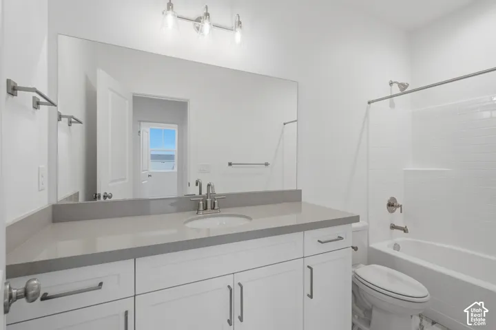 White vanity with grey stone countertop, undermount sink, three-light fixture, oversized mirror, and tub-shower combination with tiled surround