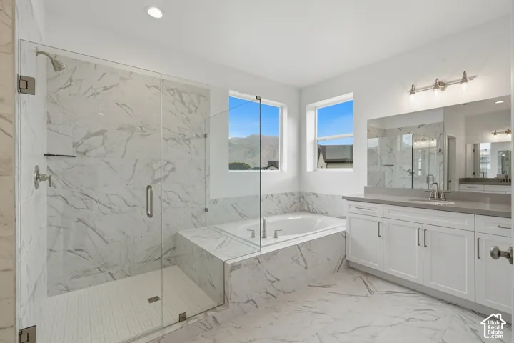 Bathroom featuring a walk-in shower with glass enclosure, soaking tub with stone-finish surround, white cabinetry, dual-basin vanity, and mountain backdrop