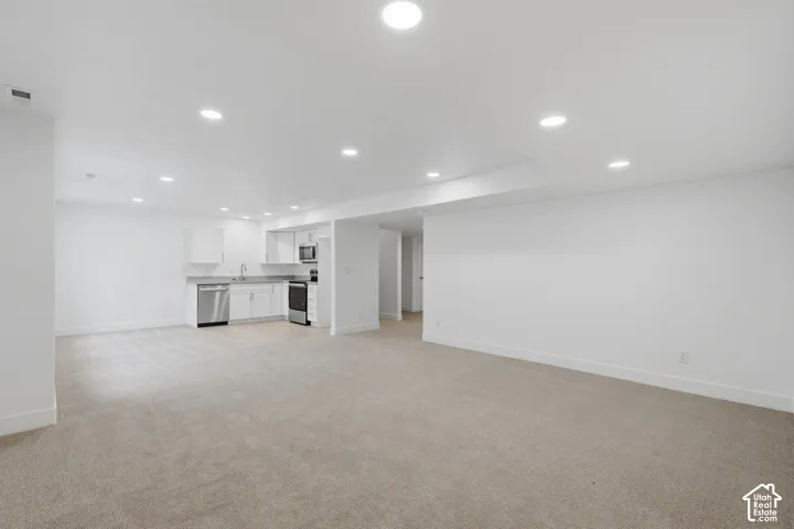 Open concept interior featuring recessed lighting, wall-to-wall carpeting, and a kitchen area with white cabinetry, stainless steel appliances, and a solid surface countertop