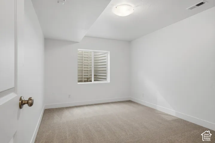 Neutral-toned carpeting, window with corrugated metal window well, and flush-mount ceiling lighting