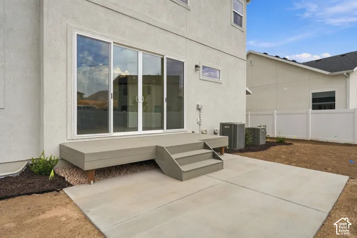 Stucco exterior featuring large sliding glass doors, a raised wooden deck with integrated steps, a poured concrete patio, and white vinyl privacy fencing