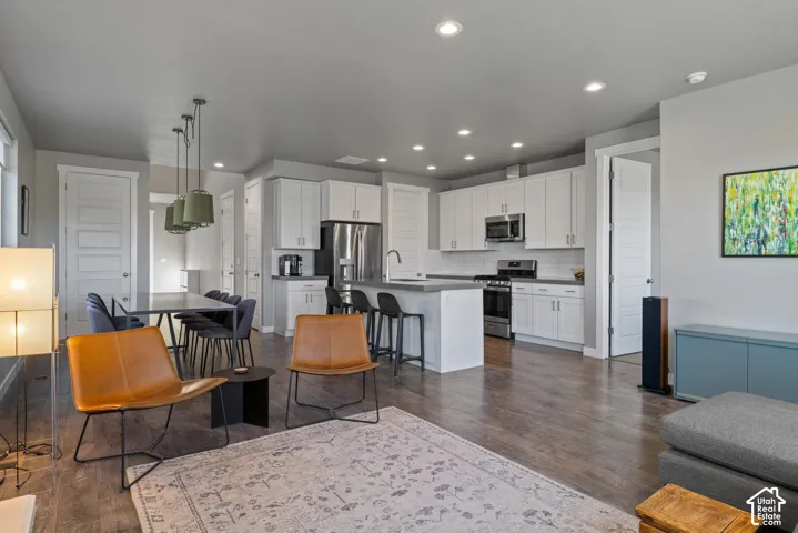 Open-concept kitchen featuring white shaker-style cabinetry, stainless steel appliances, a central island with a solid surface countertop, and wood-finish flooring throughout