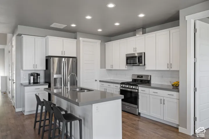 Kitchen featuring white shaker-style cabinetry, solid-surface countertops, wood-finish flooring, recessed lighting, and stainless steel appliances