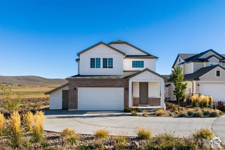 Two-story residence featuring white horizontal siding, a brick facade, a concrete driveway, a covered front entryway, and a mountainous backdrop