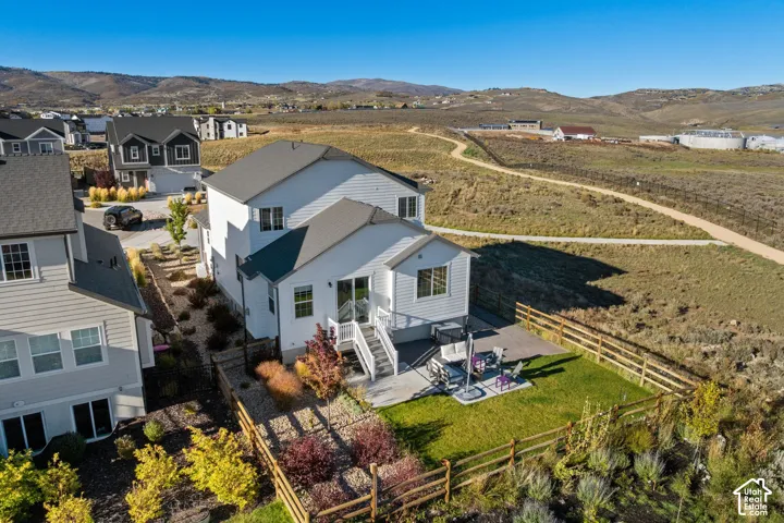 Two-story residence featuring horizontal siding, a rear concrete patio, a railed staircase, and a fenced yard with established landscaping and mountain scenery