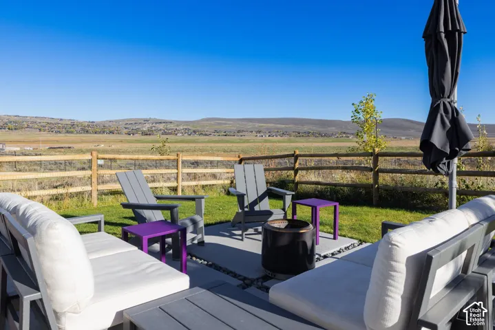 Concrete patio with inset river rock detailing, level grass lawn, post-and-rail wood fencing, and distant mountain backdrop