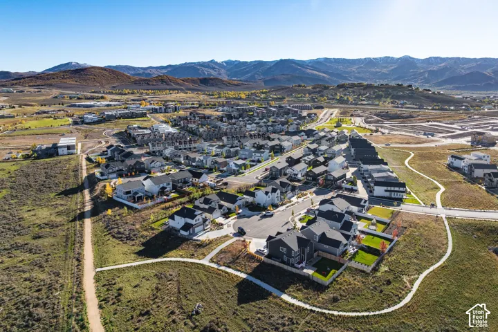 Aerial perspective featuring a residential community with paved roadways, managed green space, multi-level structures, and prominent mountain backdrops