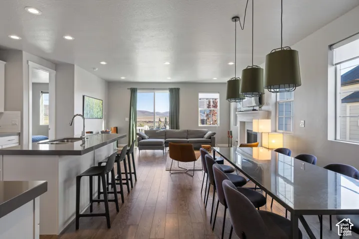 Open-concept interior featuring wood-finish flooring, recessed lighting, a kitchen island with stone-finish countertops, three suspended drum pendant lights, and a fireplace with a mantel