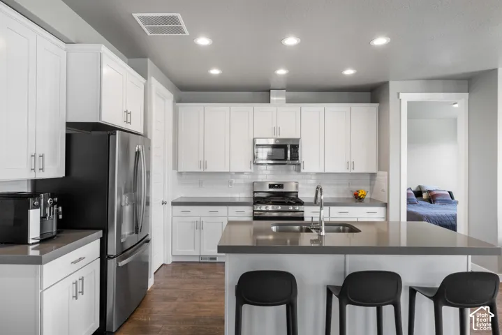 Kitchen featuring white shaker-style cabinetry, solid-surface countertops, subway tile backsplash, stainless steel appliances, and wood-finish flooring