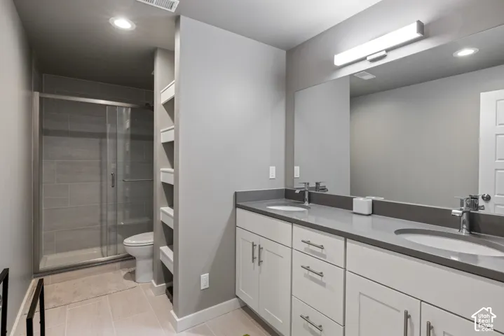 Bathroom featuring a double vanity with stone-composite countertop, integrated dual sinks, white shaker-style cabinetry, a full-width mirror with linear lighting, and a glass-enclosed shower with tile surround